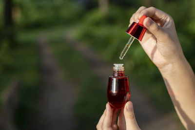 Selective focus red facial serum bottle in asian woman's hand nature background