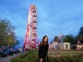 Full length portrait of smiling young woman at amusement park against sky