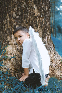 Boy looking away against tree trunk