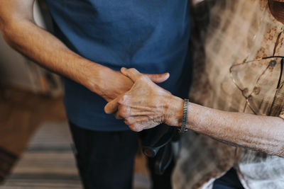 Midsection of male healthcare worker holding hand of senior woman at home