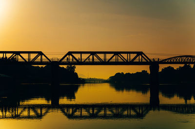 Silhouette bridge over river against sky during sunset