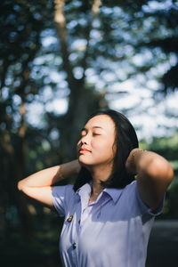 Beautiful young woman with eyes closed standing against trees