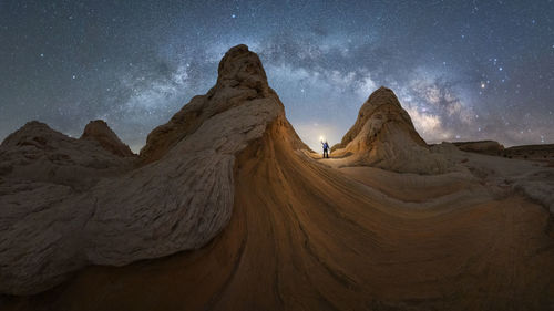 Silhouette of unrecognizable explorer standing with flashlight on scenery of rocky formations in highlands under milky way starry sky in vermillion cliffs national monument, arizona in usa