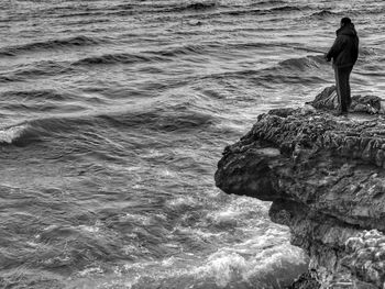 Rear view of man standing on rock in sea