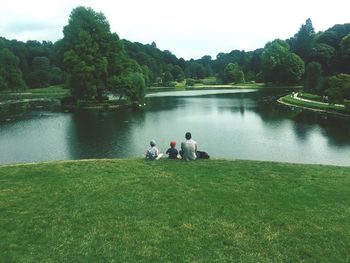 People sitting by lake against sky