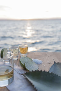 Close-up of tequila shots by lemon and salt on table by beach against sky