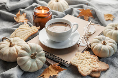 White pumpkins, coffee and autumn leaves on a grey knitted sweater. autumn home decor.