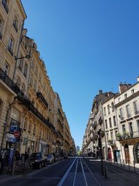 Road amidst buildings against clear blue sky