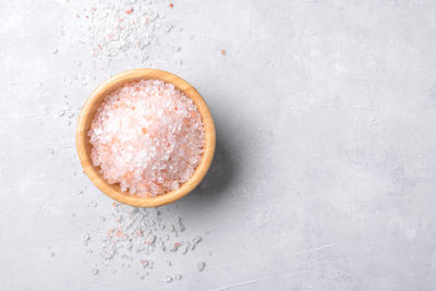 Pink himalayan salt in a wooden bowl with scattered salt on a light grey background, top view