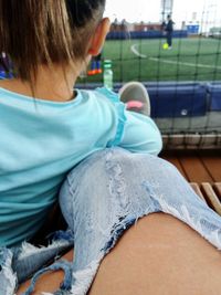 Low section of woman wearing torn jeans by girl at playing field