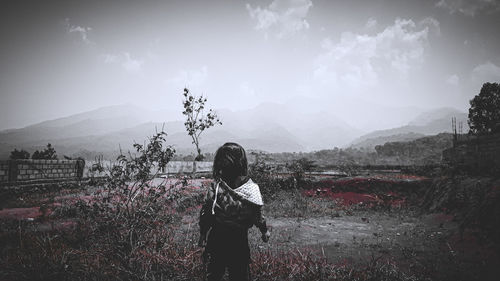 Rear view of woman standing on field against sky