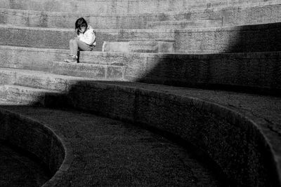 Woman sitting on staircase against wall