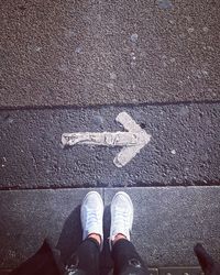 Low section of man standing on footpath by arrow symbol