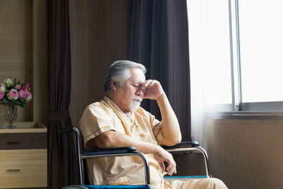 Man looking away while sitting on chair against window