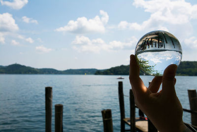 Cropped hand holding crystal ball against lake