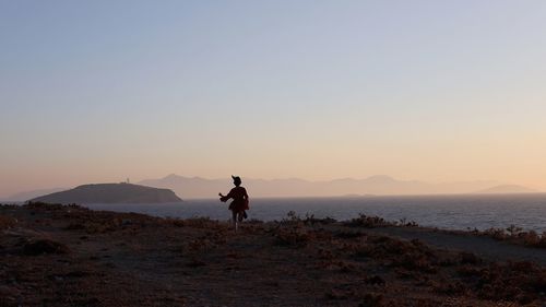 Silhouette woman standing on land against sky during sunset