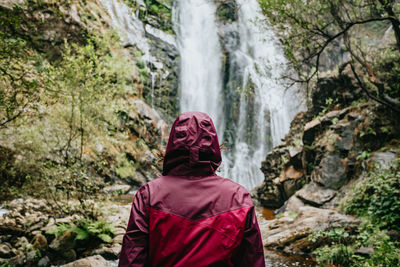 Rear view of man looking at waterfall in forest