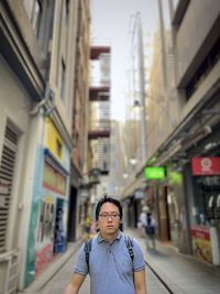 Portrait of young asian man standing against buildings in alleyway in the city.
