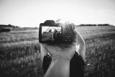 Cropped hand photographing woman making heart shape on field