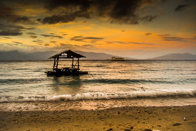 Silhouette lifeguard hut on beach against sky during sunset