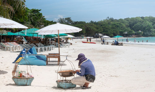 The male vendor sells the local food on the balance basket on the beach for travellers 