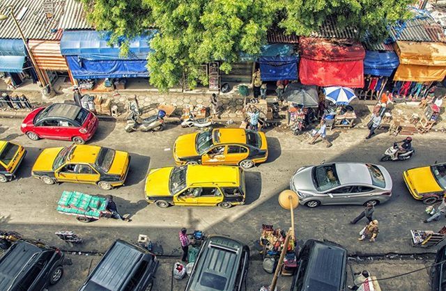 transportation, land vehicle, mode of transport, car, street, city, road, building exterior, in a row, built structure, parking, architecture, tree, city life, incidental people, high angle view, stationary, city street, day, sunlight