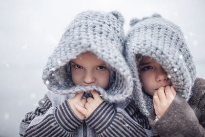 Girl in knitted grey hat hugging her frozen smaller brother