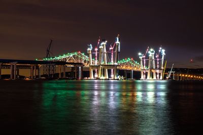 Illuminated city by sea against sky at night