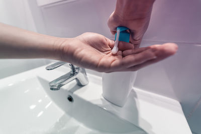 Close-up of hand holding faucet in bathroom