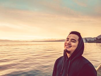 Smiling man in hooded shirt against sea at sunset