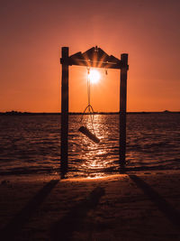 Silhouette of wooden swing on sea with sky at sunset
