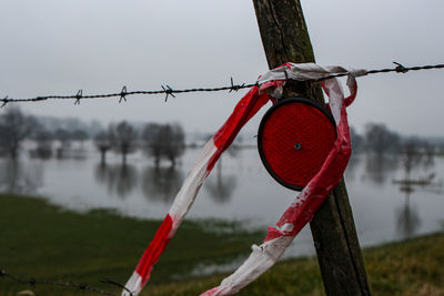 Close-up of red barbed wire hanging on fence against lake