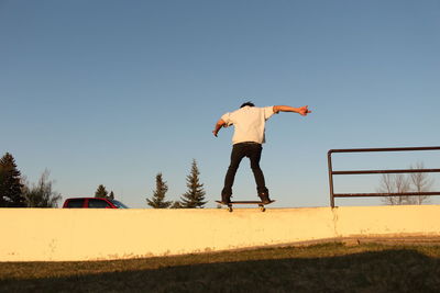 Rear view of man skateboarding by railing against clear sky