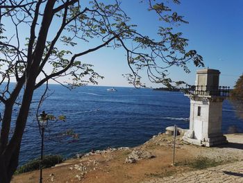 Lighthouse by sea against blue sky