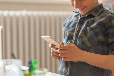 Close up of happy boy reading a text message on cell phone at home. copy space.