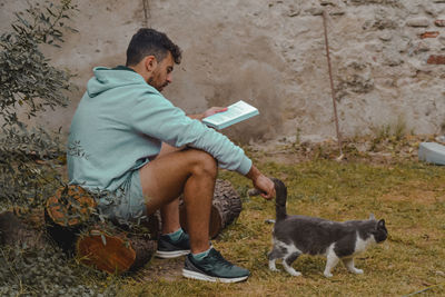 Side view of man holding cat sitting outdoors