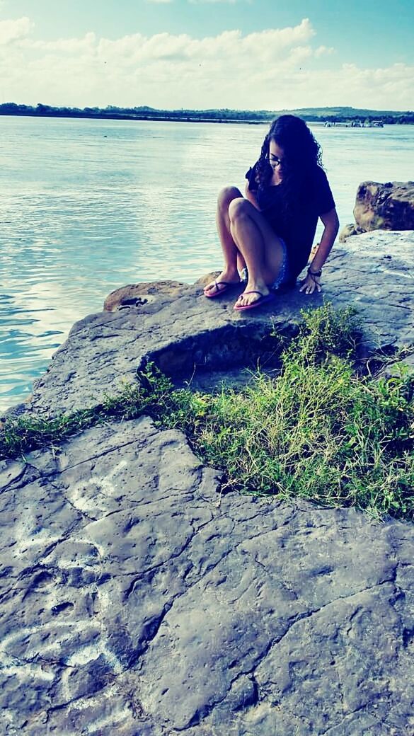 water, one person, leisure activity, sitting, real people, lifestyles, young adult, nature, young women, beach, sea, land, day, relaxation, sky, full length, solid, rock, outdoors, contemplation, hairstyle