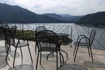 Empty chairs and table by lake against mountains