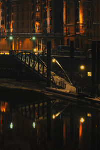 Illuminated bridge over river by buildings in city at night