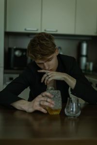 Teenage boy with drink sitting in kitchen at home