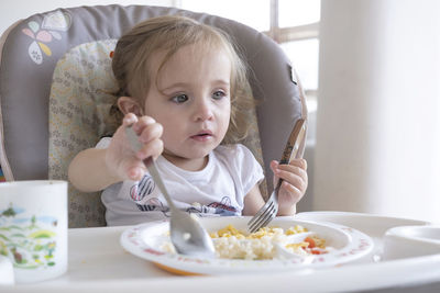 Little girl eating alone in the chair by the table.