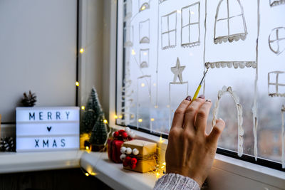 Female hand draws christmas holidays decoration painted on window glass. new years scenery. city 