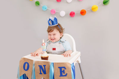 Cute baby boy sitting against wall during birthday