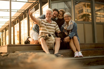 Senior man taking selfie of happy family sitting in steps