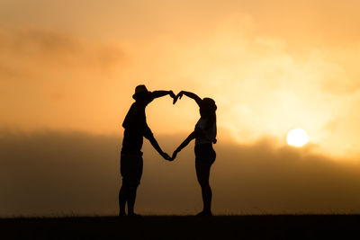 Silhouette couple standing on field against sky during sunset