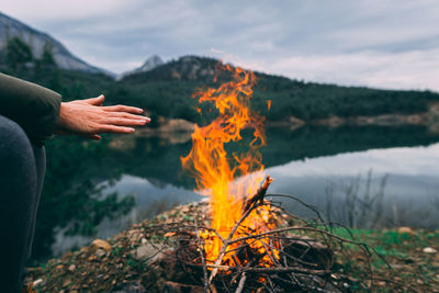 Midsection of woman by fire and lake against sky