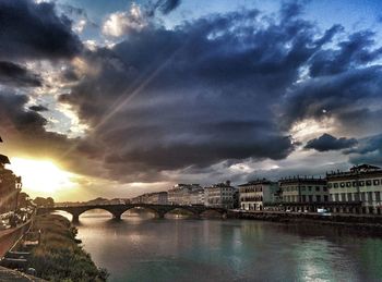 Bridge over river in city against cloudy sky