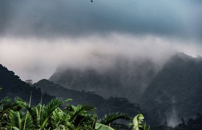 Scenic view of rocky mountains against cloudy sky during foggy weather