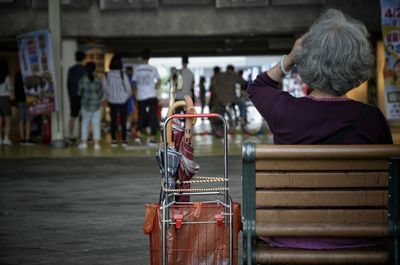 Rear view of women sitting with luggage and umbrellas on bench