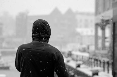 Rear view of man standing against buildings in snow covered city
